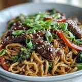 Garnished with green onions and sesame seeds, this Korean Beef Noodles bowl is served steaming hot for a comforting meal.