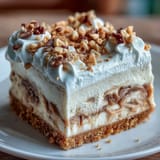 Freshly whipped cream and chopped peanuts top a rich slice of Nutter Butter cheesecake on a white plate.