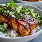 Bang Bang Salmon Bowl with crispy salmon, vibrant cucumber-edamame salsa, and sesame seeds, served ready to eat with lime wedges.