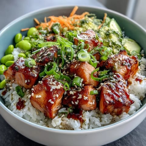 Golden baked salmon cubes sit on fluffy white rice with crisp cucumber and bright carrot shreds. The Baked Salmon Rice Bowl is drizzled with creamy sriracha mayo for a spicy kick. Fresh avocado and green onions add color and creamy texture to this healthy dinner.