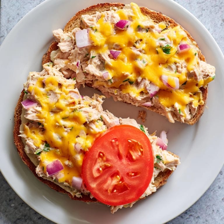 Warm tuna melt sandwich on toasted bread, overflowing with creamy tuna and cheese, ready to eat.