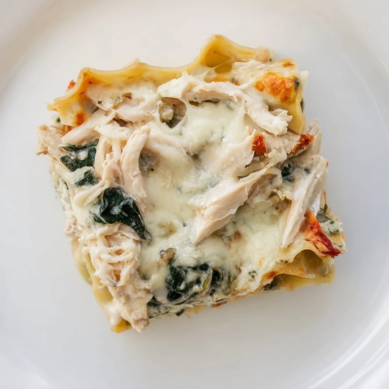 Freshly baked Chicken Alfredo Lasagna served in a white dish with herbs, perfect for a comforting family dinner.
