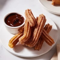 Golden, crispy churros dusted in cinnamon sugar, next to a decadent dark chocolate dipping sauce.