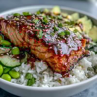 Flaky glazed salmon and creamy avocado sit atop fluffy jasmine rice in a vibrant Honey Sriracha Salmon Bowl.