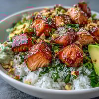 Freshly seared salmon nestled in sushi rice with creamy avocado slices, spicy chili oil drizzle, and crunchy chopped peanuts.
