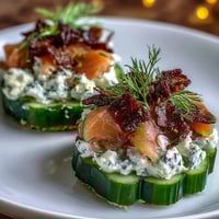 Crisp cucumber rounds topped with creamy dill-infused cheese and delicate smoked salmon, garnished with fresh dill and capers.